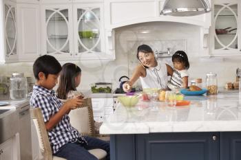 Busy Mother Organizing Children At Breakfast In Kitchen