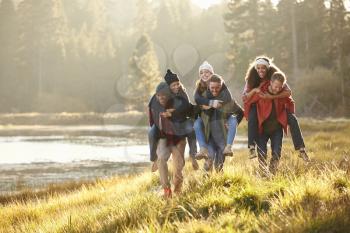 Six friends have fun piggybacking in the countryside by lake