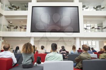 Students watching big screen in university atrium, back view