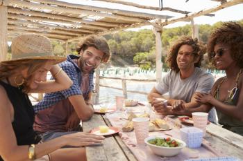 Four friends talking at a table by the sea, side view, Ibiza