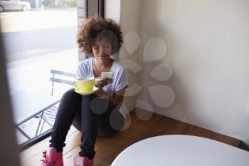 Young black woman sitting by window in cafe using smartphone