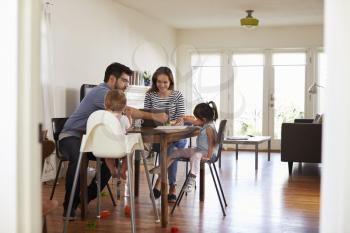 Mother Uses Laptop Whilst Father Plays With Children At Home