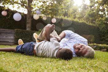 Grandfather and grandson play lying on grass, low angle