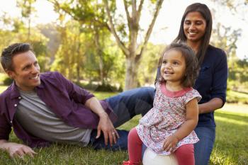 Mixed race parents and young daughter sit in park, close up
