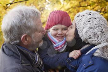 Mother And Grandfather Cuddle Girl On Autumn Walk