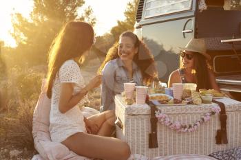 Three female friends enjoying a picnic by their camper van