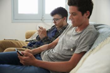 Two teenage boys relax, messaging friends with smartphones