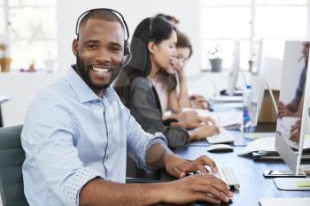 Young black man with headset on smiling to camera in office