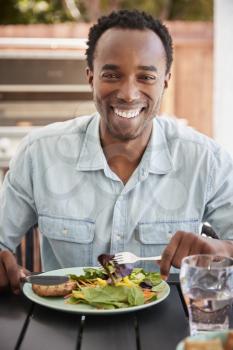 Young black man eating lunch at a table outside, vertical