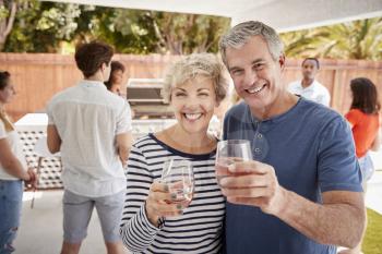 Senior couple at a backyard party raising glasses to camera