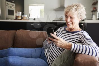 Senior white woman sitting on couch at home using smartphone