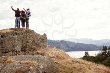 A group of five young adult friends embrace with arms in the air after arriving at summit during mountain hike, back view