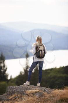 A young adult Caucasian woman standing alone on the rock after hiking, admiring lake view, back view