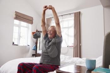 Senior Man Waking Up And Stretching In Bedroom