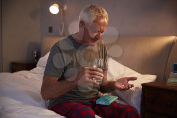 Senior Man Sitting On Bed At Home Taking Medication