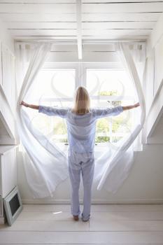 Rear View Of Woman Opening Curtains And Looking Out Of Window