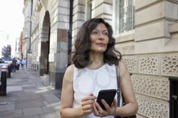 Woman in street navigating with smartphone, looking ahead
