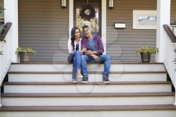 Couple Sitting On Steps Leading Up To Porch Of Home