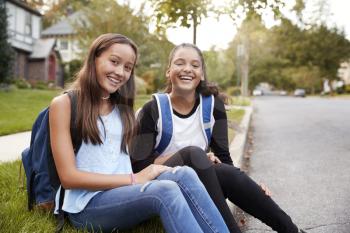 Two teen girlfriends sit at the roadside looking to camera