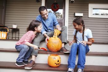Father And Daughters Carving Halloween Pumpkin On House Steps