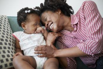 Mother Lying On Sofa At Home Playing With Baby Daughter