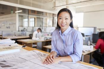 Female Asian architect smiling to camera in open plan office