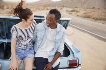 Couple Sitting In Trunk Of Classic Car On Road Trip