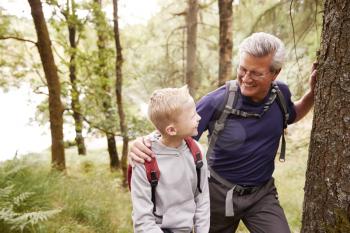 Grandfather and grandson taking a break while hiking together in a forest, close up, looking at each other