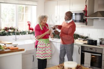 Senior black man pouring champagne for his partner in the kitchen while preparing dinner on Christmas Day, selective focus
