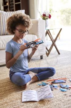 Pre-teen girl sitting on the floor in the living room building a toy from a construction kit, close up, vertical