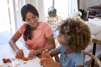 Two young teen and pre-teen girlfriends sitting at a table at home playing with modelling clay, close up, elevated view