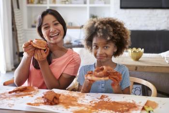 Two girlfriends having fun playing with modelling clay, holding up their creations and showing them to camera, close up