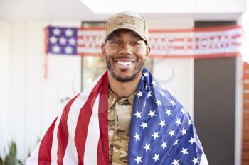 Millennial black soldier with US flag draped over his shoulders, smiling to camera, close up