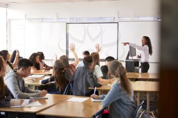 Female High School Teacher Asking Question Standing By Interactive Whiteboard Teaching Lesson