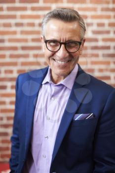 Portrait Of Smiling Mature Businessman Standing Against Brick Wall In Modern Office