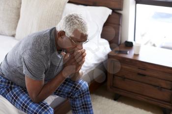 Depressed Senior Man Looking Unhappy Sitting On Side Of Bed At Home With Head In Hands