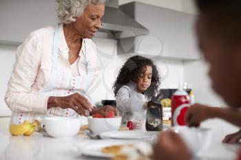 Grandmother In Kitchen With Grandchildren Making Pancakes Together