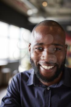 Mid adult black male creative sitting in an office social area, head and shoulders close up, vertical, crop