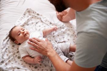 Close Up Of Loving Father Lying With Newborn Baby On Bed At Home In Loft Apartment