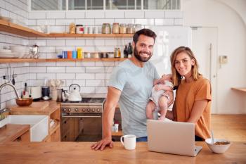 Portrait Of Busy Family In Kitchen At Breakfast With Father Caring For Baby Son