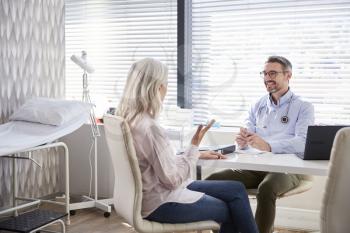 Mature Female Patient In Consultation With Doctor Sitting At Desk In Office