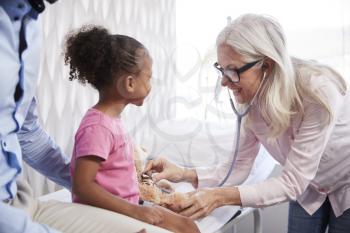 Female Doctor Giving Teddy Bear Medical Exam On Family Consultation In Office