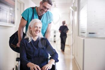 Male Orderly Pushing Senior Female Patient Being Discharged From Hospital In Wheelchair