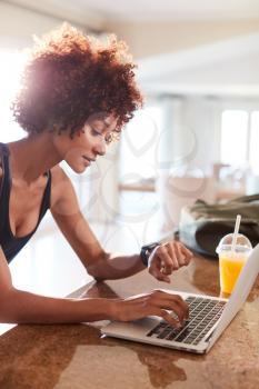 Millennial African American woman checking fitness app on watch and laptop after workout, vertical