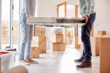 Close Up Of Couple In New Home On Moving Day Carrying Table Together