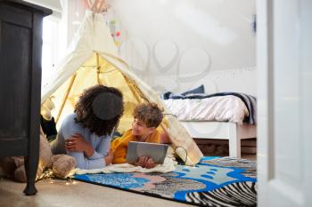 Single Mother Playing With Son On Digital Tablet In Den In Bedroom At Home
