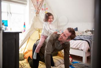 Daughter Riding On Fathers Back As They Play In Den In Bedroom At Home