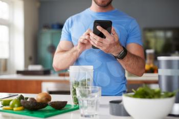 Close Up Of Man Using Fitness Tracker To Count Calories For Post Workout Juice Drink He Is Making