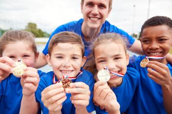 Portrait Of Children With Male Coach Showing Off Winners Medals On Sports Day