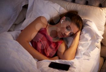 Woman Sleeping In Bed Wearing Wireless Earphones Connected To Mobile Phone